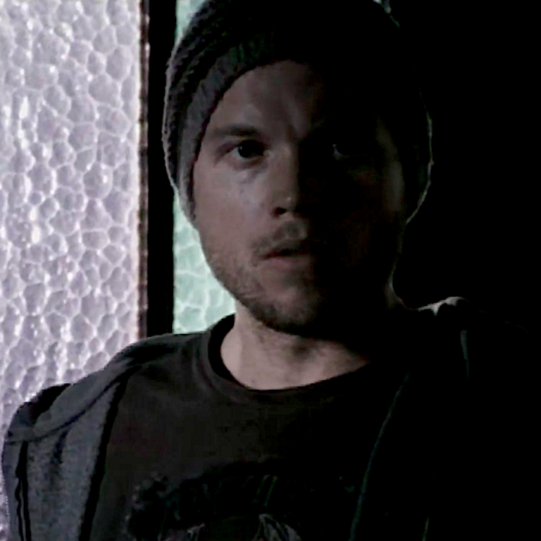 A young man with a beanie standing in front of a glass door.